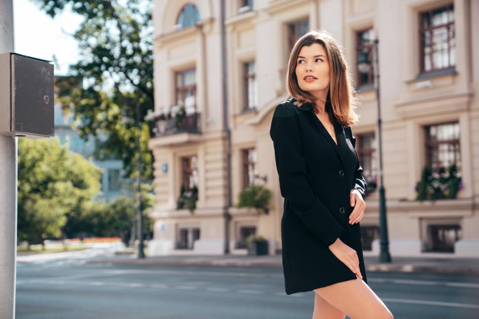 Free Image of Woman in stylish black coat poses confidently on city street in bright daylight, showcasing modern urban fashion 