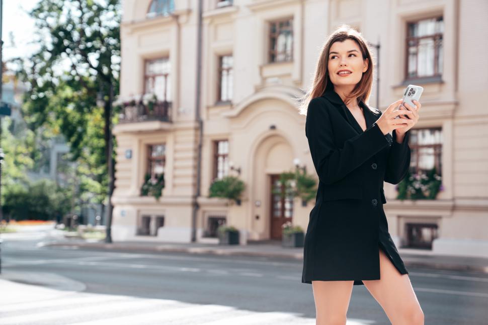 Free Image of Stylish woman walking on the street holding a smartphone near an elegant building on a sunny day 