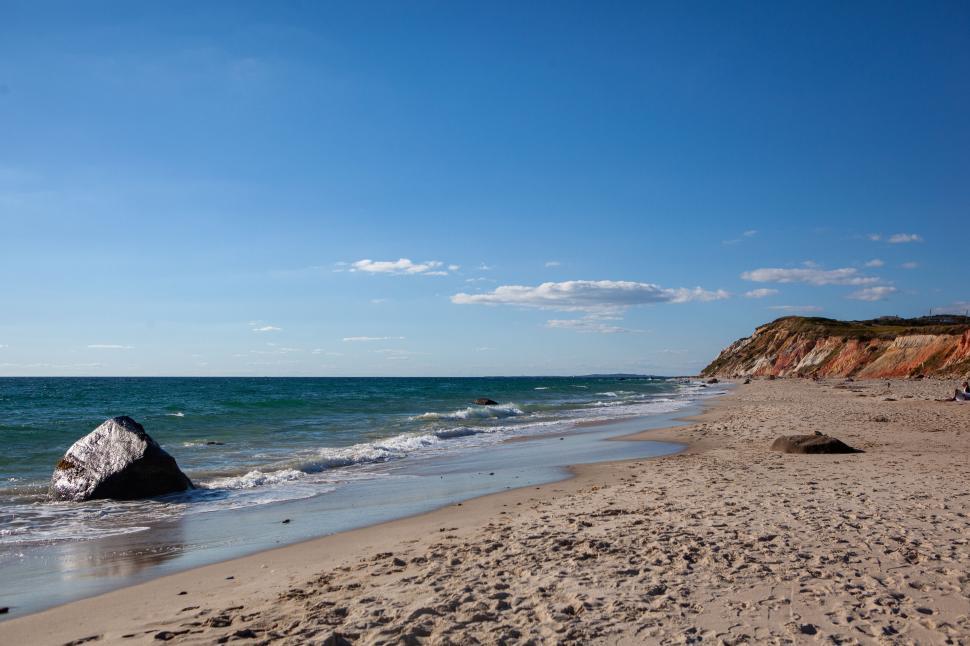 Free Image of Sunny beach with waves crashing and a distant cliff 