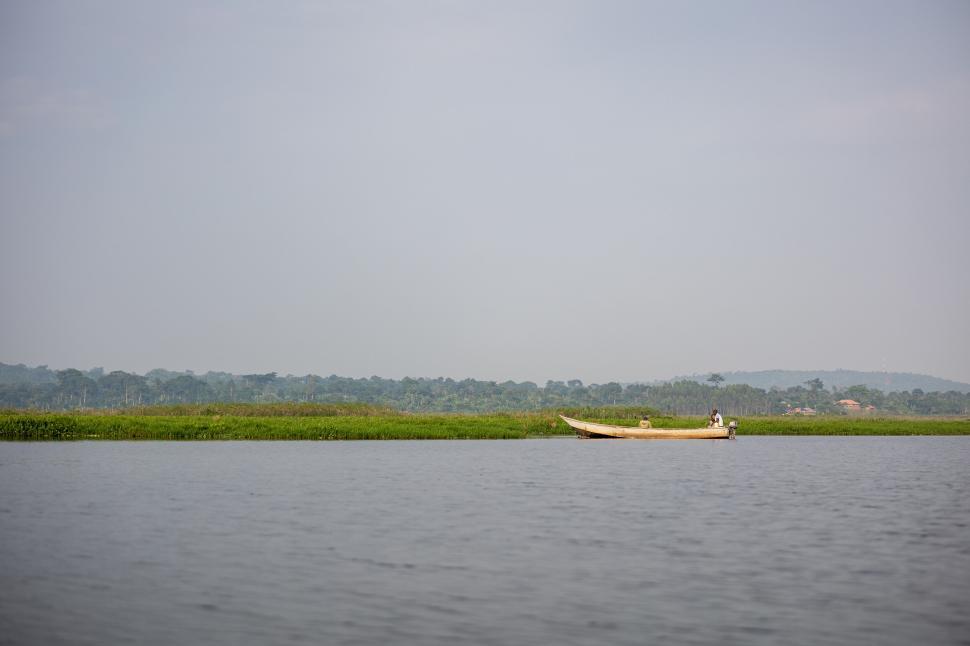 Free Image of Wooden boat on calm lake with lush green shore, clear sky 