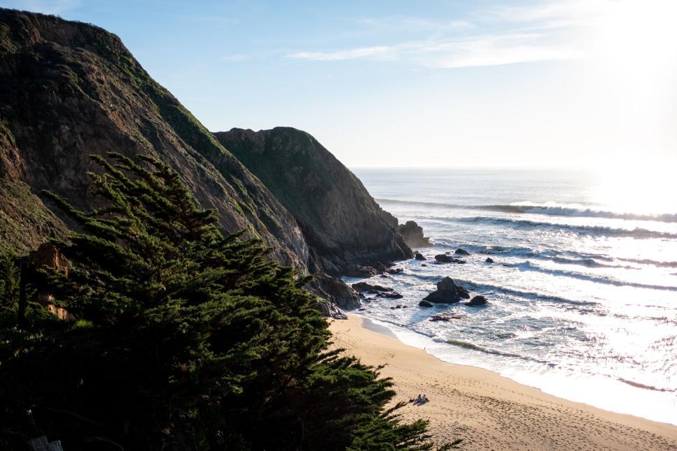 Free Image of Sunlit beach with rocky shore and distant cliffs 