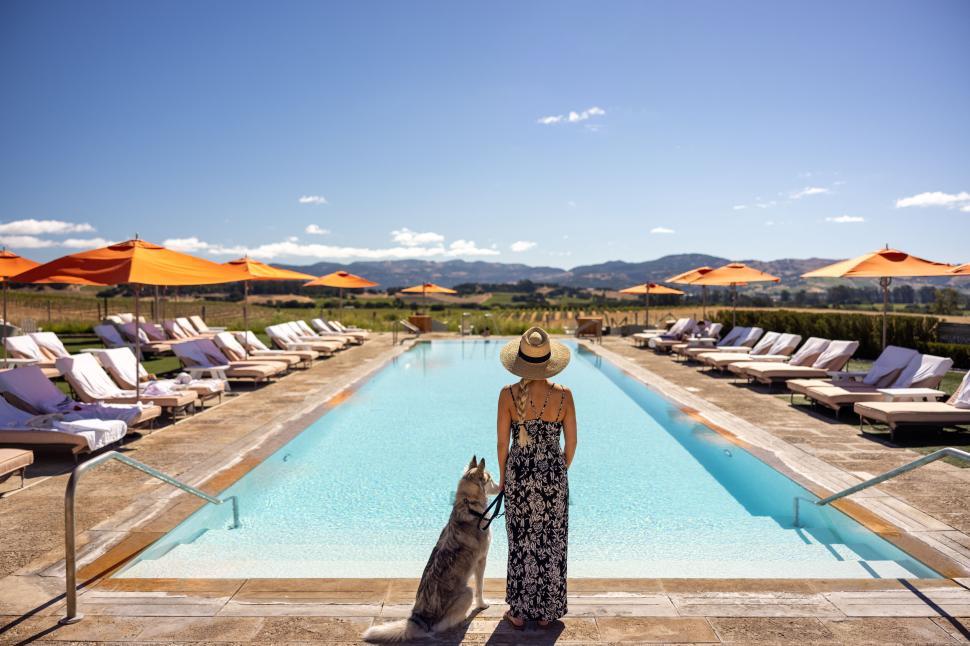 Free Image of Woman and dog by an elegant pool with orange umbrellas 