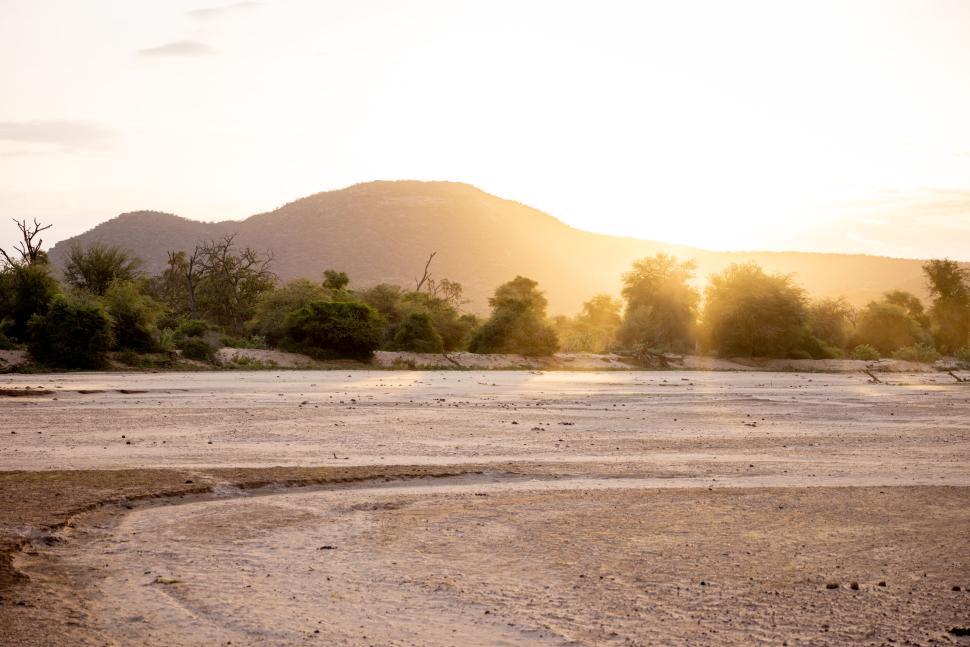 Free Image of Sunset over arid landscape with sparse trees and hills 