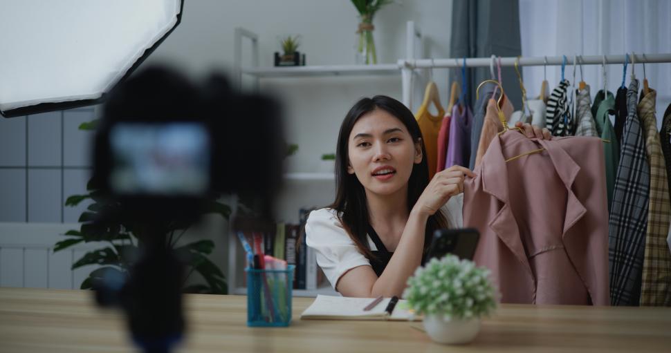 Free Image of Young Asian woman live streaming at clothes shop on digital camera 