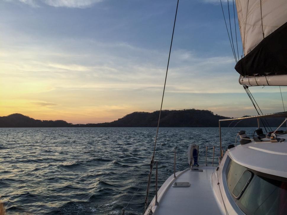 Free Image of Sailboat on the ocean at sunset with hills in view 