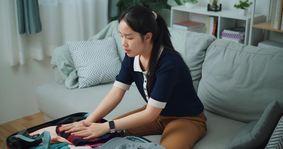 high-angle-view-of-asian-teenager-woman-sitting-on-sofa-packing-travel-luggage.jpg