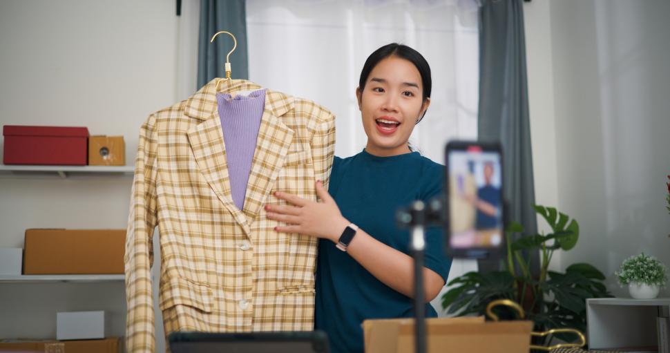 Free Image of Portrait of Young asian woman business owner stand selling clothes live streaming on mobile phone show new collection fashion clothes to customer ,Online Shopping 