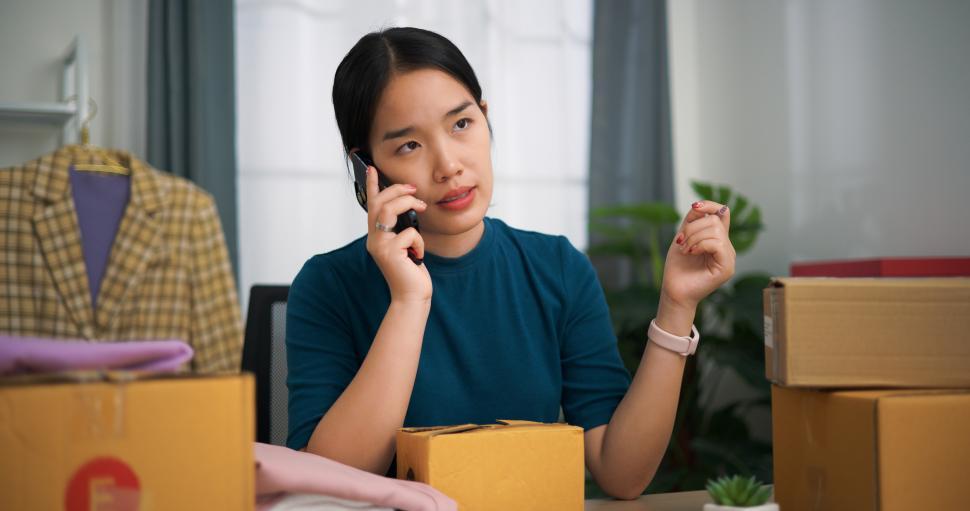 Free Image of Portrait of Young asian woman business owner sitting at desk talking with customer on smartphone while packing for shipping, Online Shopping 