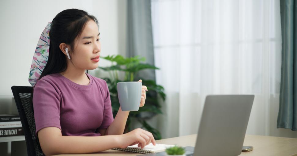 Free Image of Portrait of Young asian business woman wear wireless headphones drink coffee while using laptop for video conference call presenting project plan to colleagues at home office, online meeting for remote work 