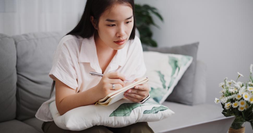 Free Image of High angle view, Young asian woman take notes while meeting online on laptop on sofa in the living room at home ,Lifestyle with device technology, Working from home 