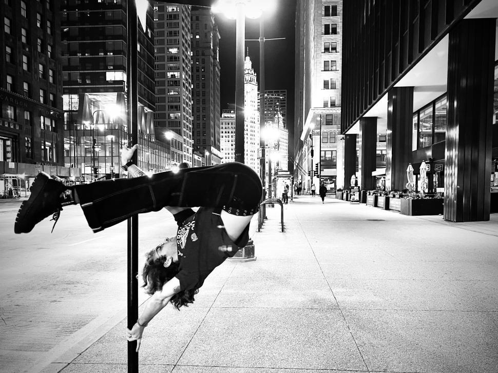 Free Image of Urban pole sport artist performs acrobatic move on street pole near Chicago city buildings at night 