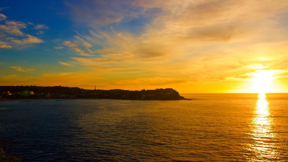 Free Image of Golden sunset over a calm ocean and dark coastline 