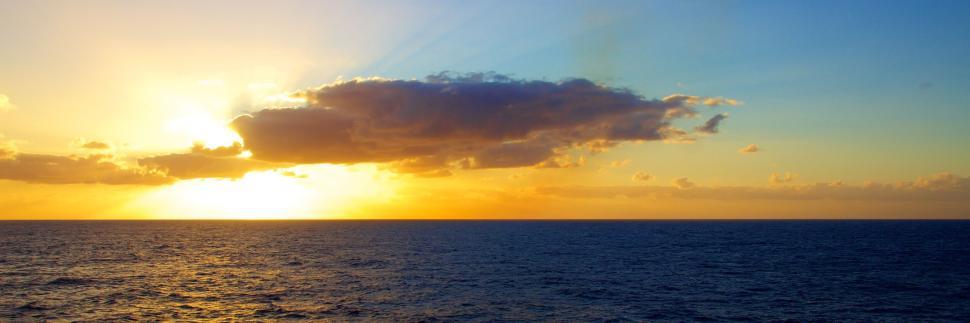 Free Image of Golden sunrise over calm ocean with scattered clouds. 