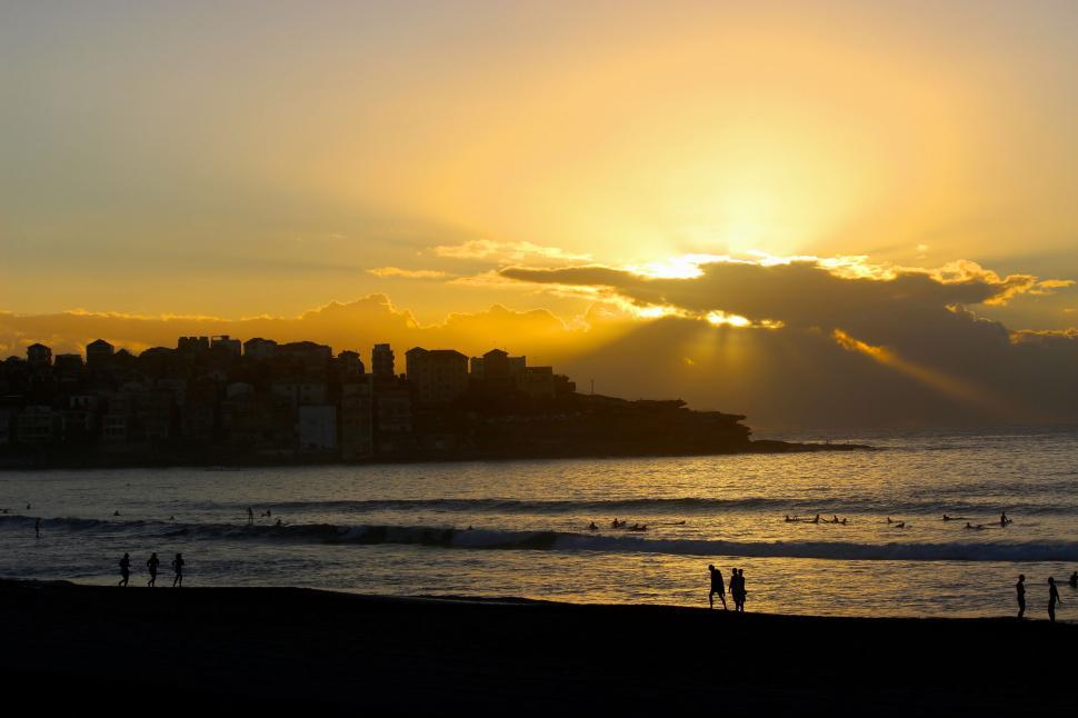 Free Image of Sunset beach with silhouetted people and distant waves. 