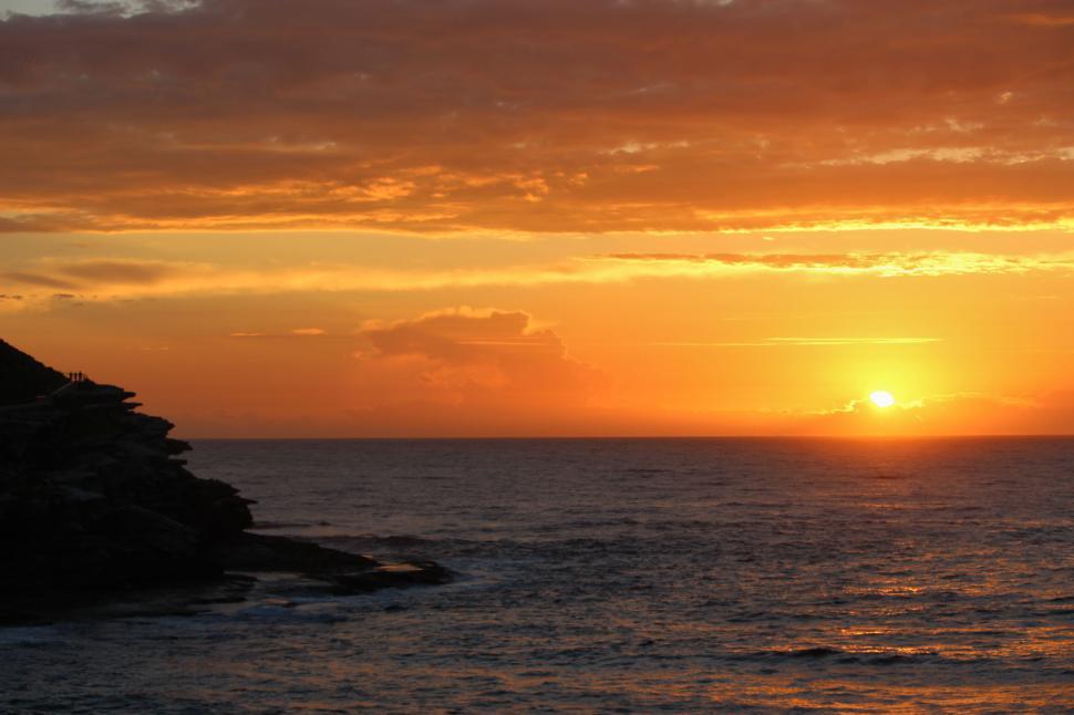 Free Image of Sun setting over the ocean with cloudy sky near coastline 