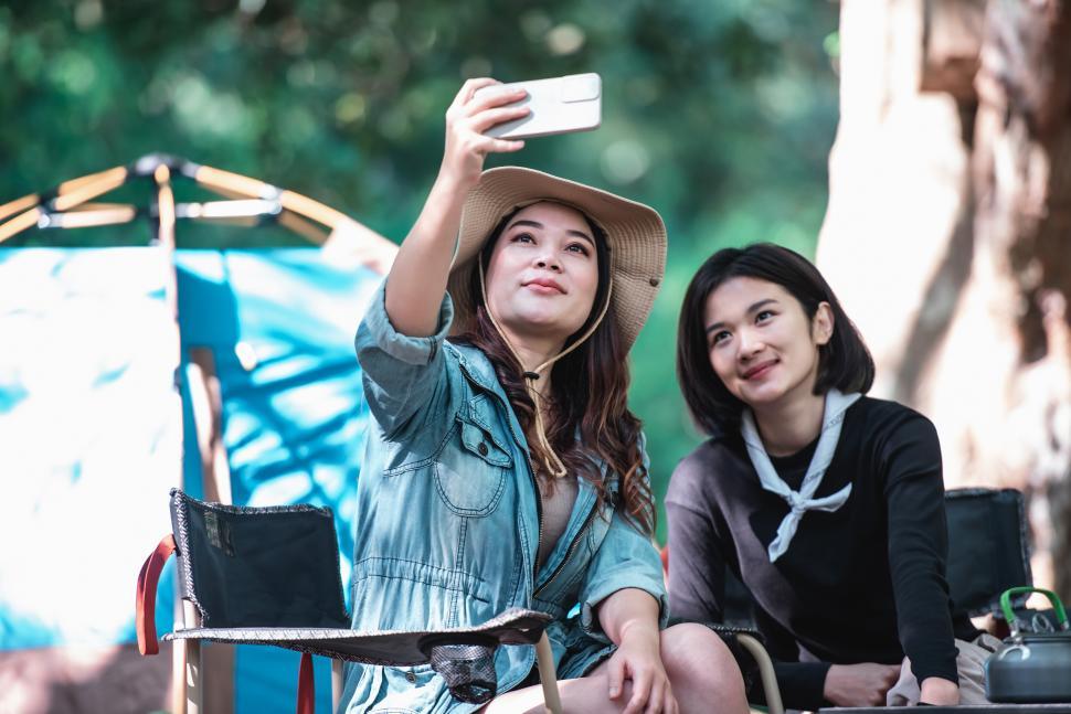 Free Image of Asian pretty woman and girlfriend use smartphone selfie on camping&x9 