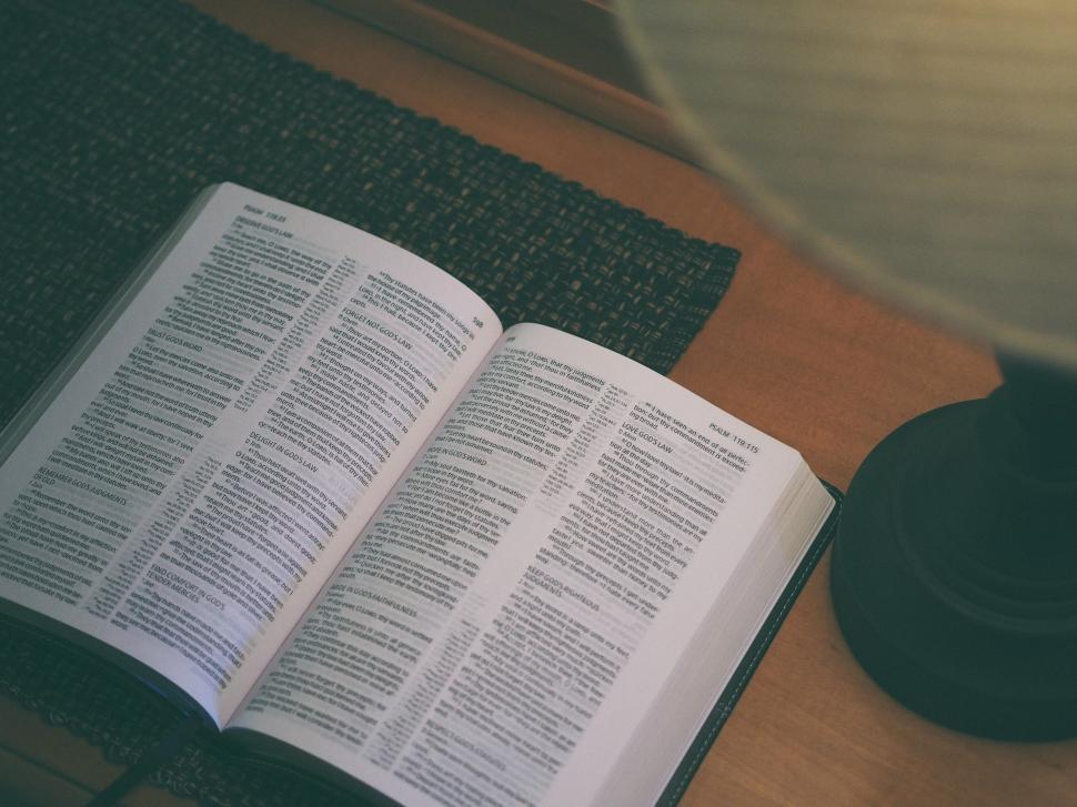 Free Image of Open book resting on a wooden table near a lamp 