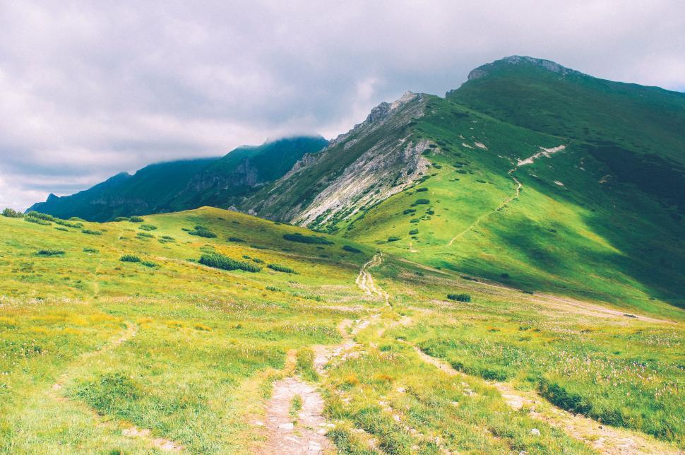 Free Image of Hiking trail on a green hillside under cloudy sky 