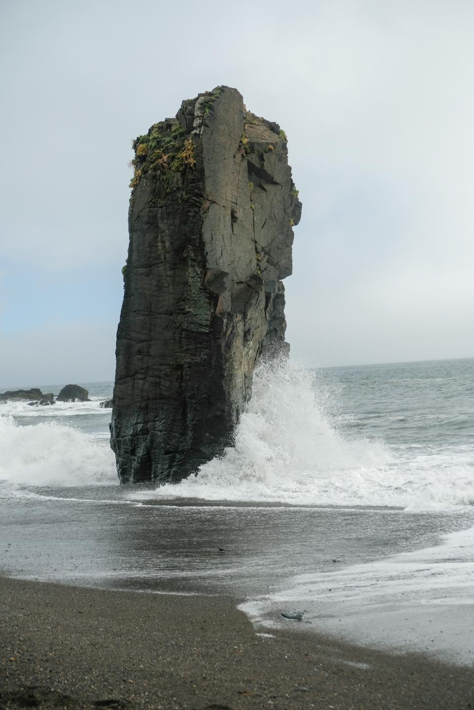 Free Image of Waves crash against a towering rock formation by the shore 