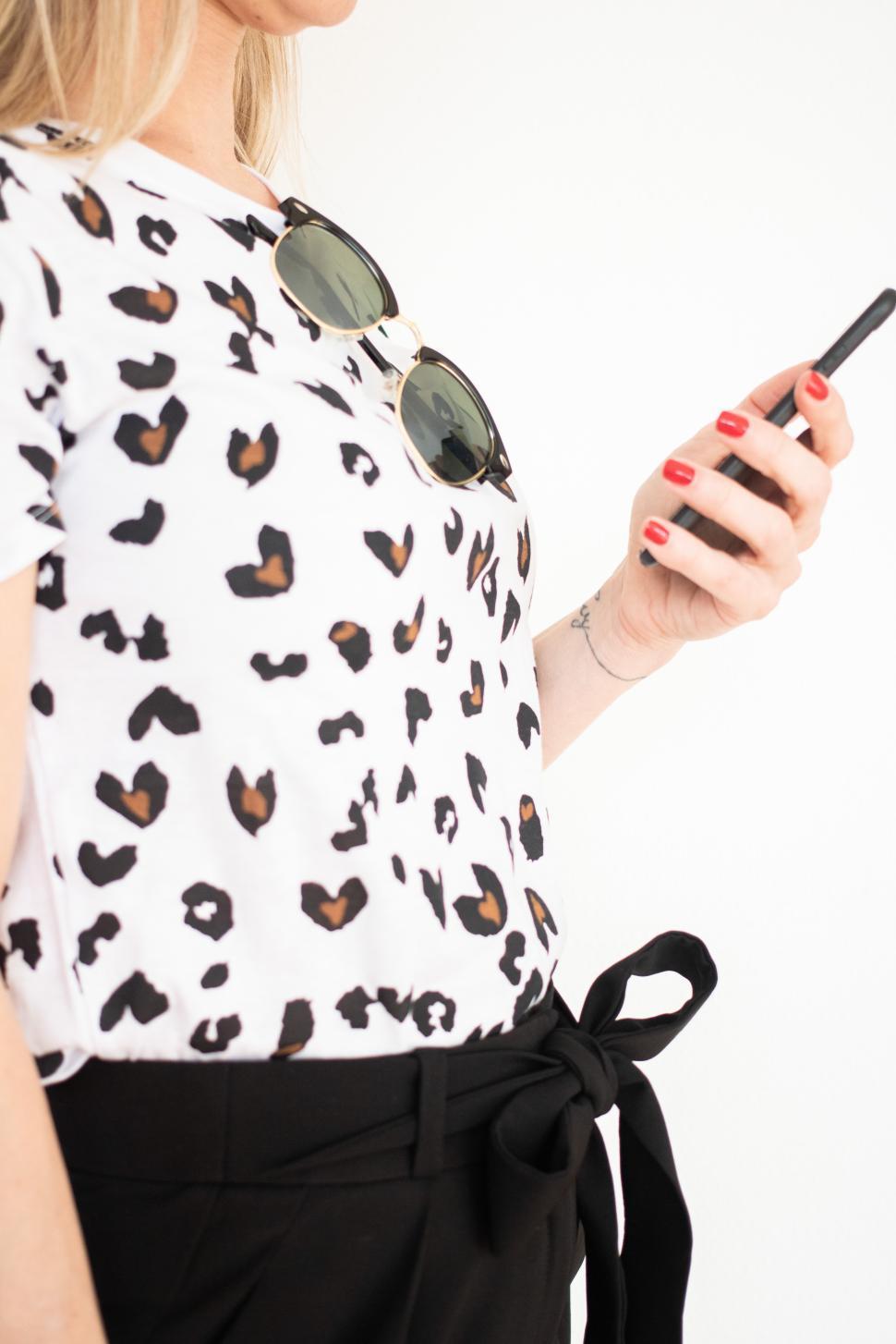 Free Image of Woman in a leopard print shirt using a smartphone 