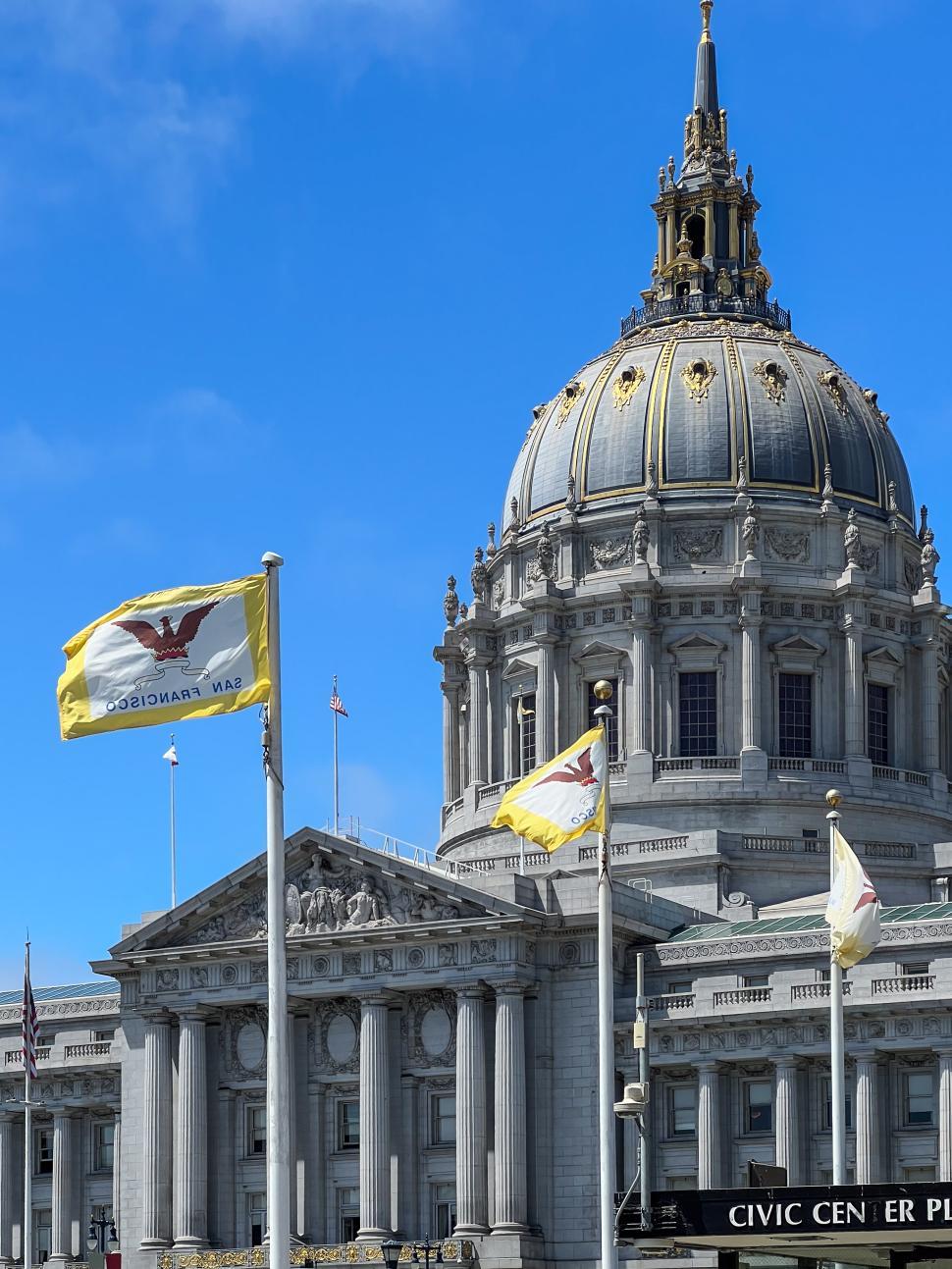 Free Image of San Francisco City Hall building with flags waving under a clear blue sky 