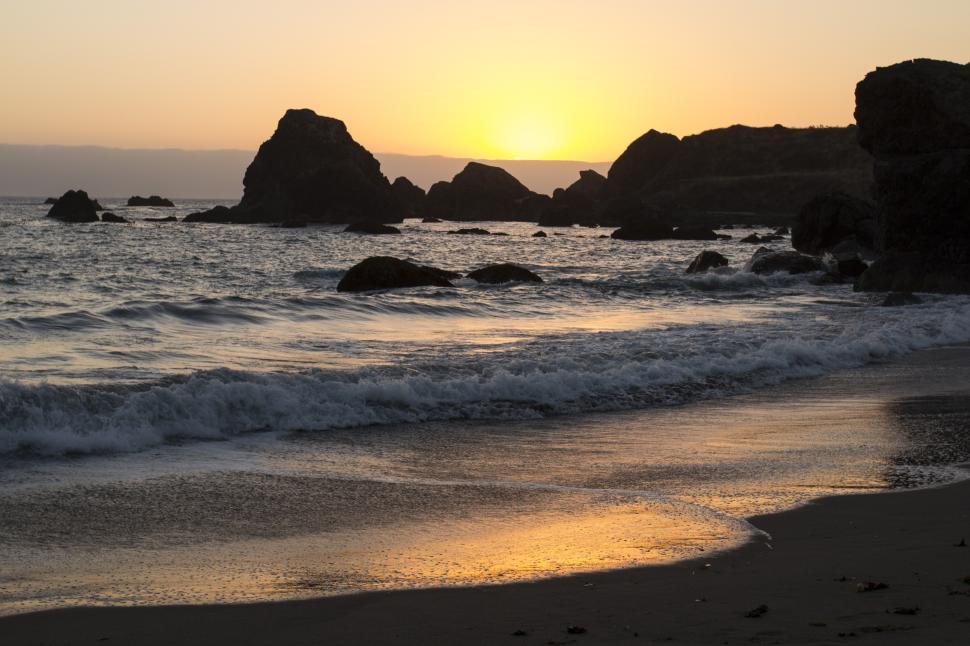 Free Image of Sunset over rocky shore with gentle waves and golden reflections 