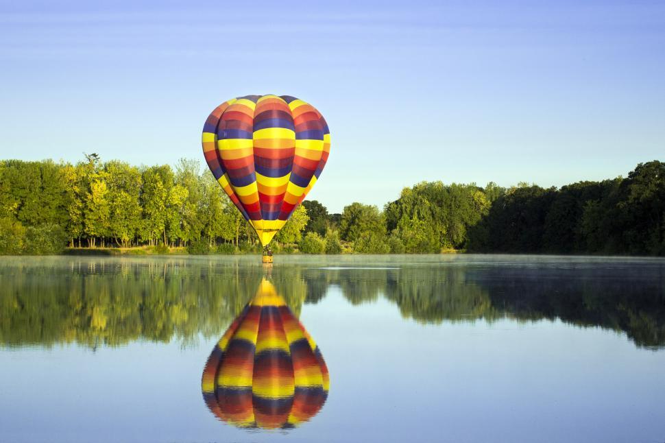 Free Image of Colorful hot air balloon floats over calm lake at sunrise 