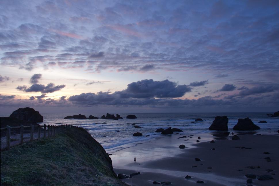Free Image of Sunset over rocky beach with solitary figure by the ocean 
