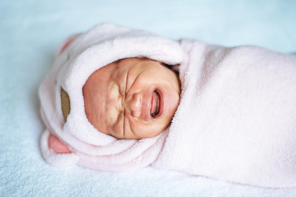 Free Image of Newborn baby wrapped in a soft pink blanket and crying 