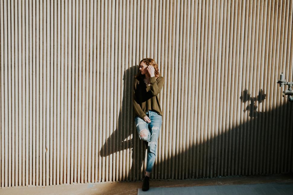 Free Image of Young woman leaning against textured wall at sunset 