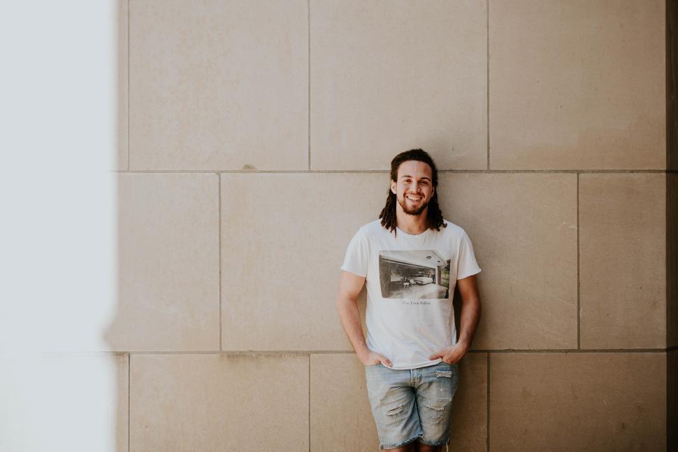 Free Image of Smiling young man leans against a textured wall 