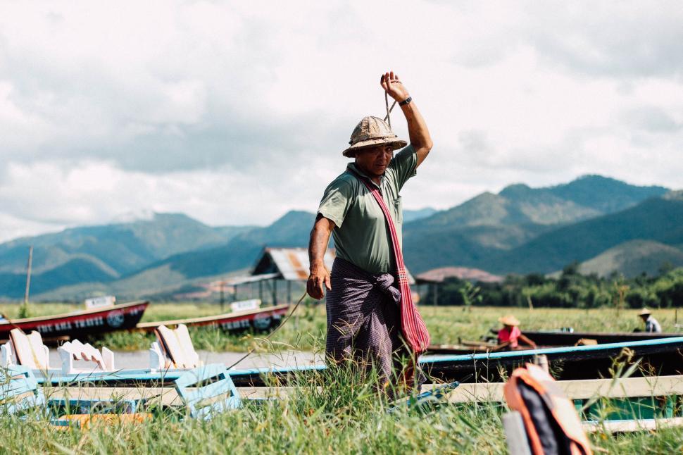Free Image of Fisherman walking along grassy shore by mountains and boats 