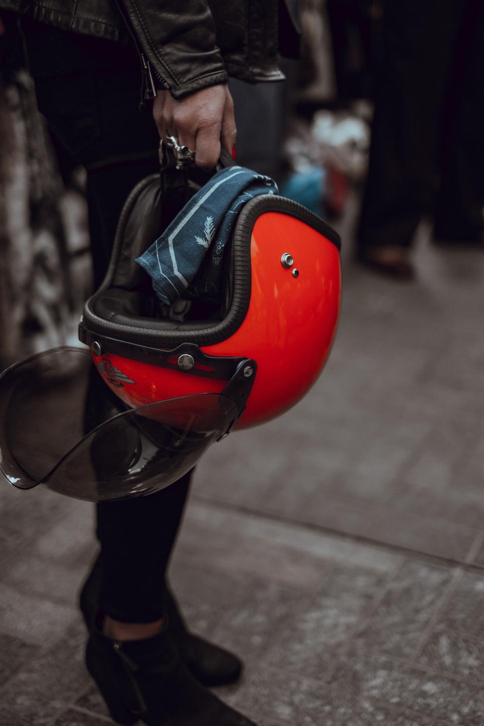 Free Image of Person holding a bright red helmet with a scarf in a busy space 