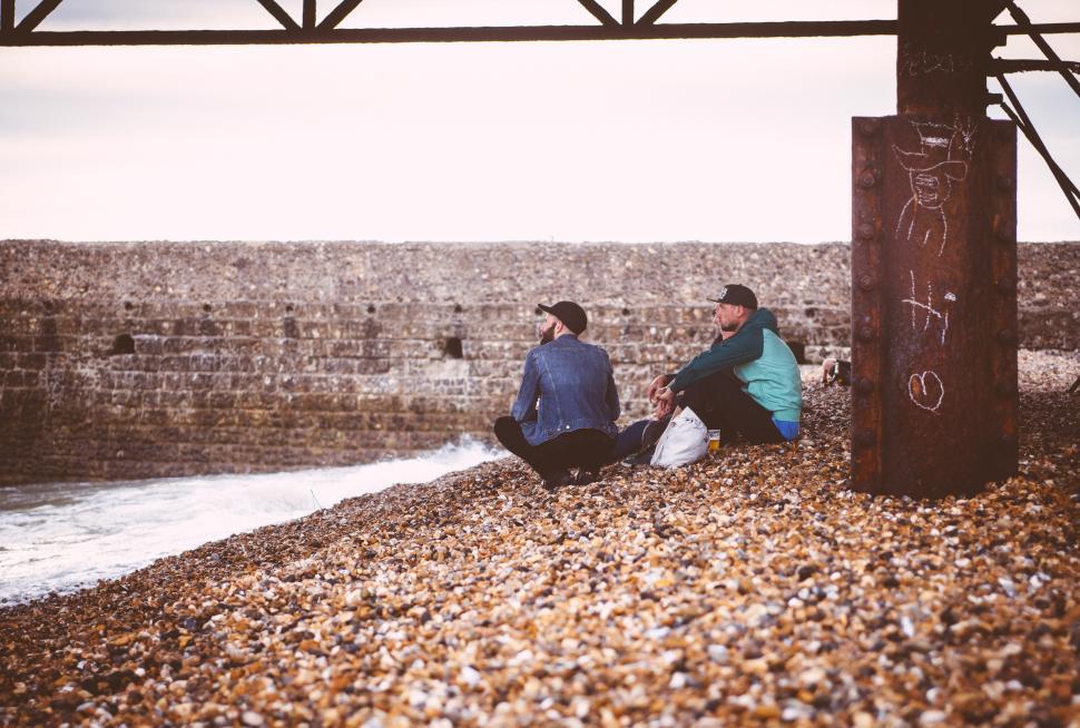 Free Image of Friends sitting on beach rocks enjoying coastal view in evening 