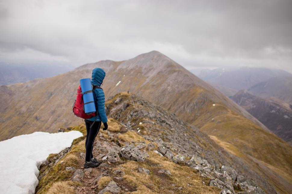 Free Image of Hiker standing on rocky ridge with mountains in background during overcast day 
