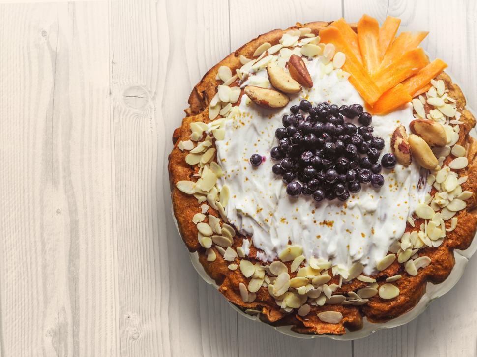 Free Image of Homemade fruit tart topped with cream, nuts, and fresh fruit on wooden table 