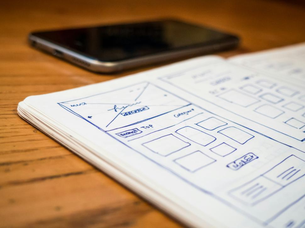 Free Image of Sketches of a mobile app layout on a wooden table near a smartphone 