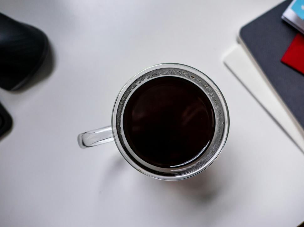 Free Image of Freshly brewed coffee in a clear mug on a white table with notebooks 