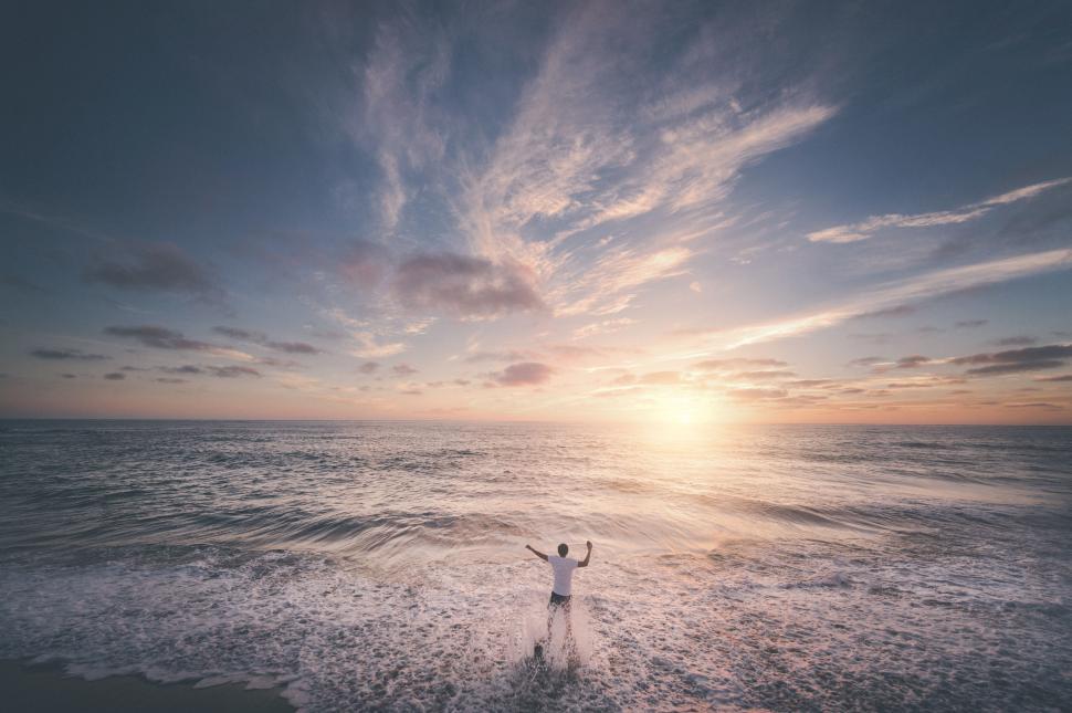 Free Image of Sunset over ocean with person enjoying the waves 