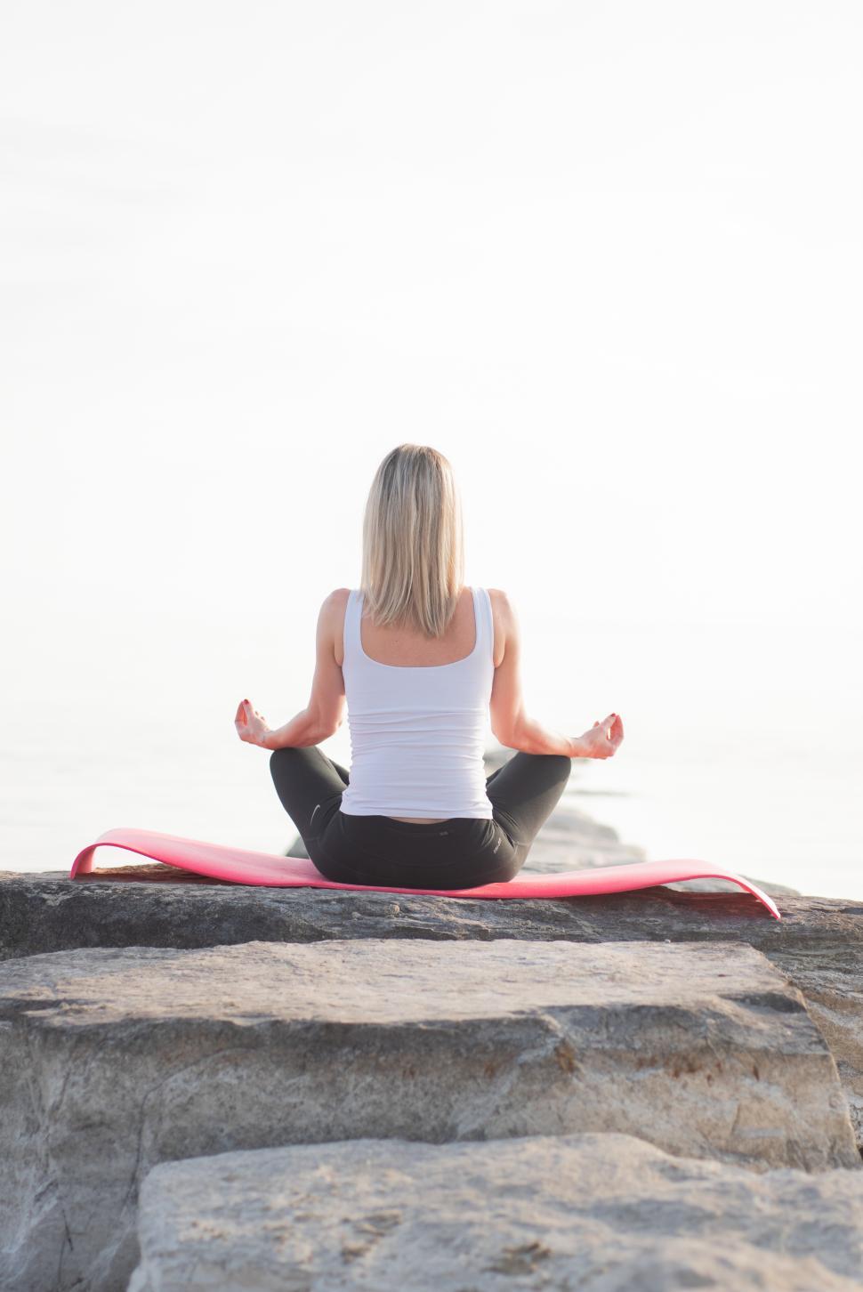 Free Image of Woman practicing yoga on a rock by the sea at sunrise 