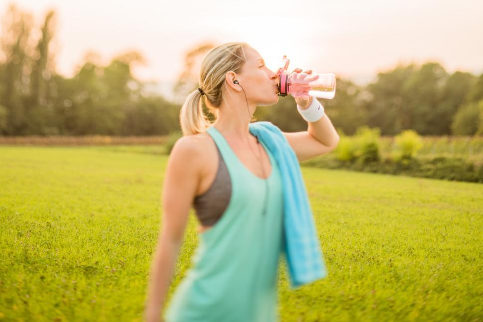 Free Image of Woman enjoying a refreshing drink in a green field 