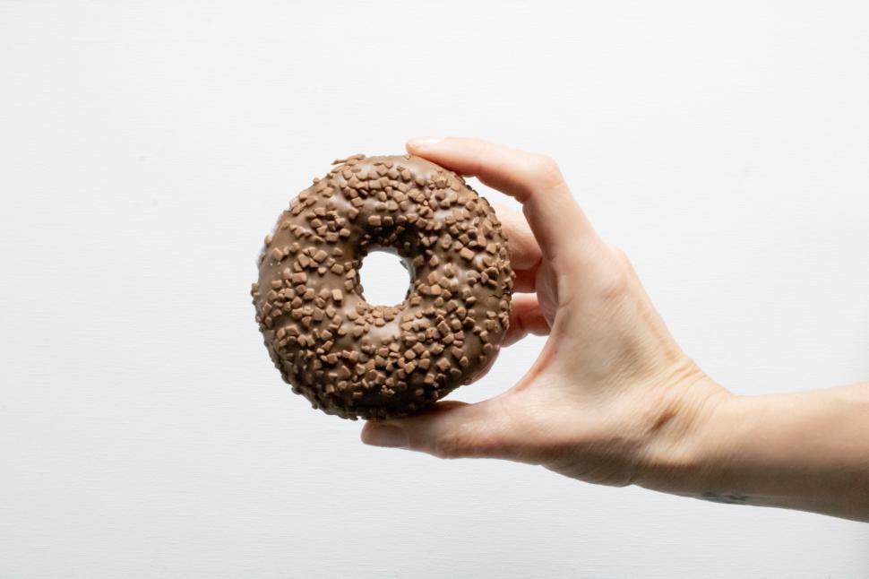 Free Image of Chocolate donut held by hand against plain background 