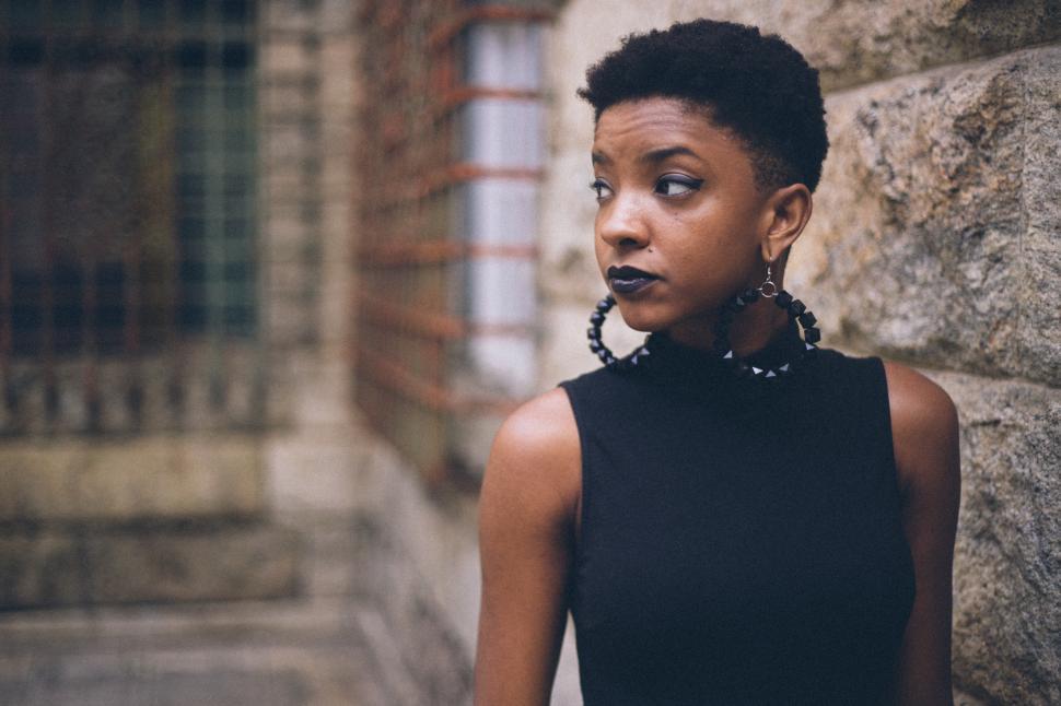 Free Image of Woman with short hair wearing earrings poses against a stone wall 