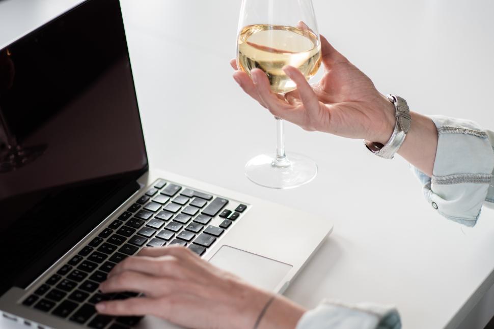 Free Image of Person working on laptop while holding a glass of wine 