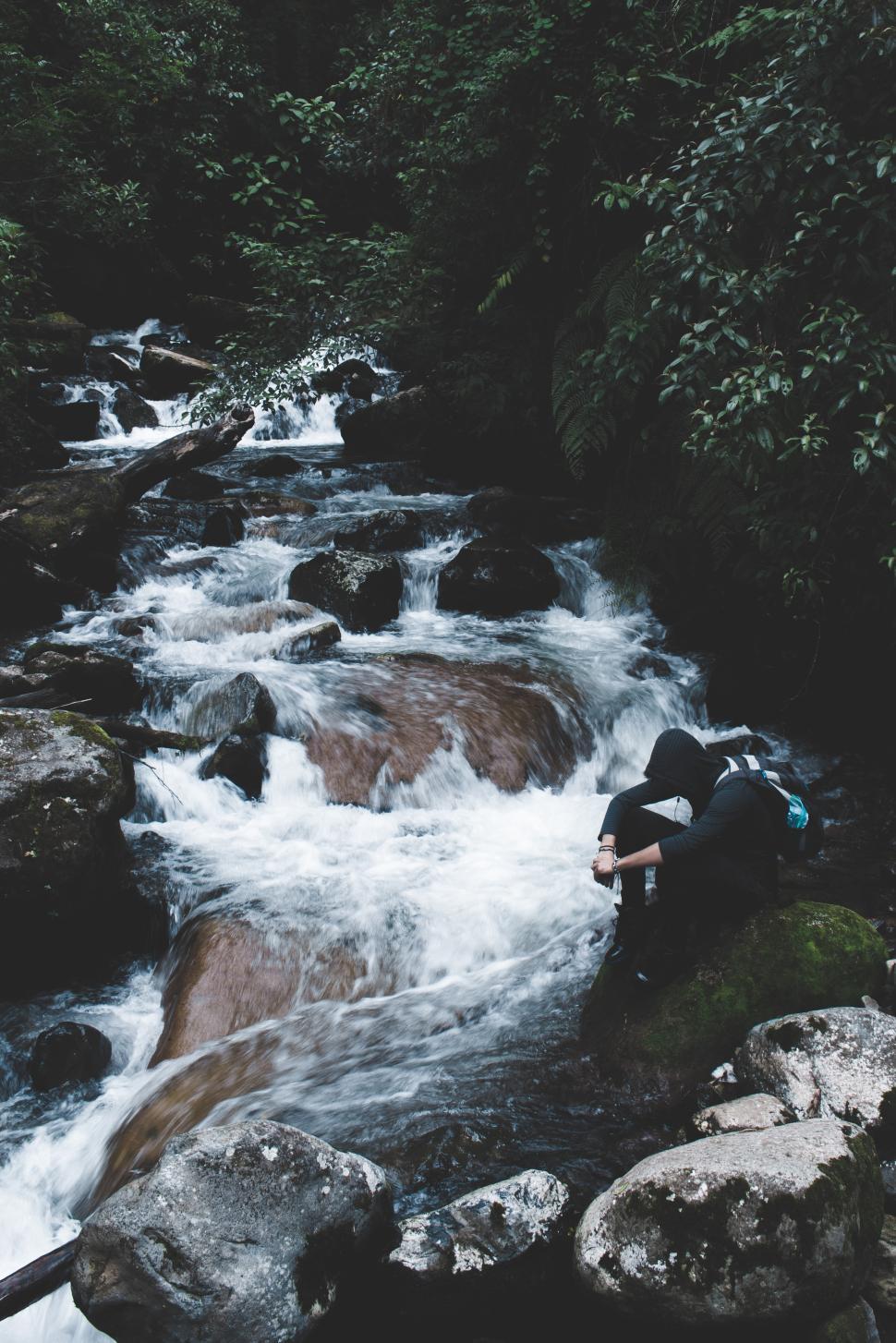 Free Image of Person resting by a flowing river in a natural setting 