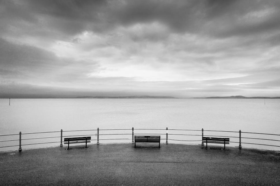Free Image of Cloudy waterfront view with benches overlooking the calm water at dusk 