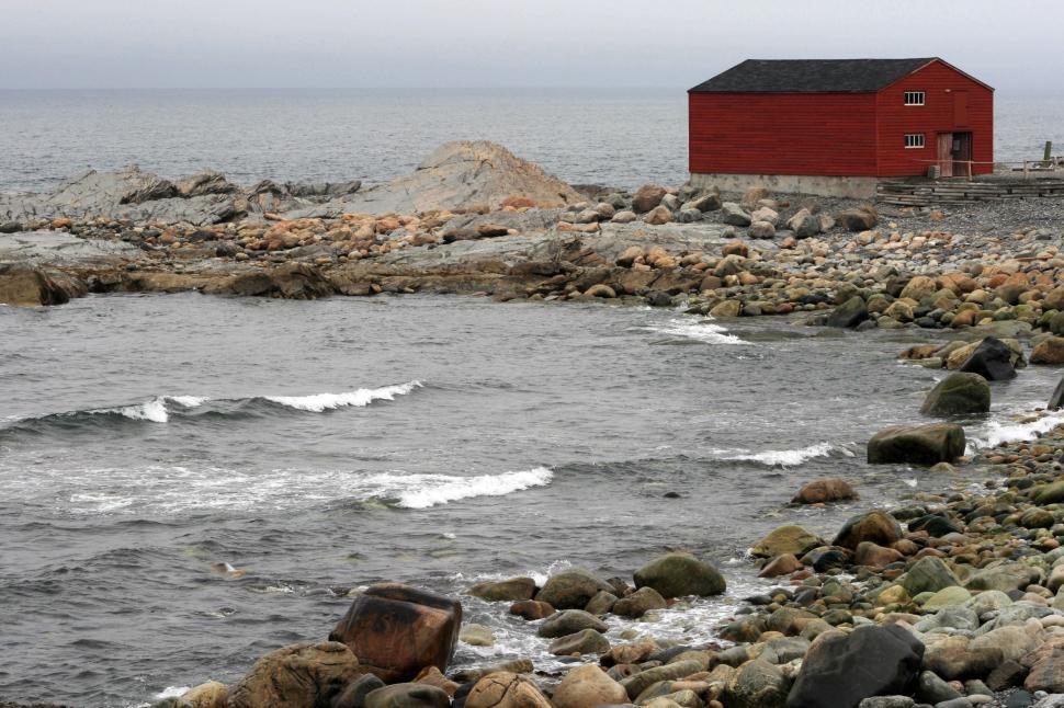 Free Image of Red cottage by rocky coastline under overcast sky 