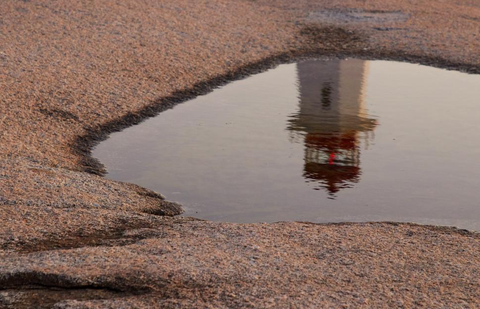 Free Image of Reflection of lighthouse in puddle on rocky surface 