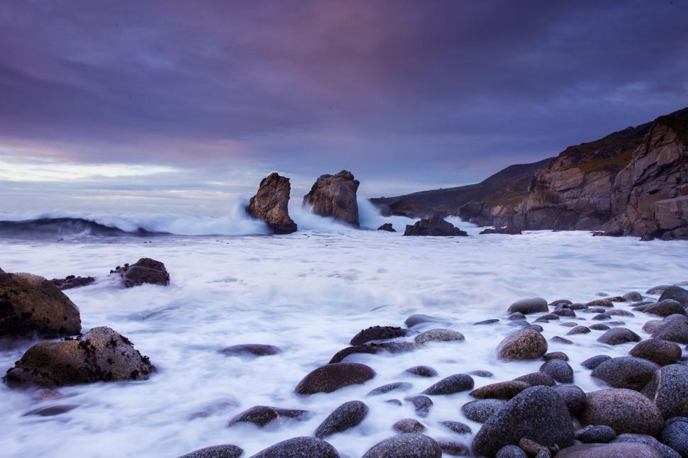 Free Image of Majestic coastal view with waves crashing against rock formations at sunset 