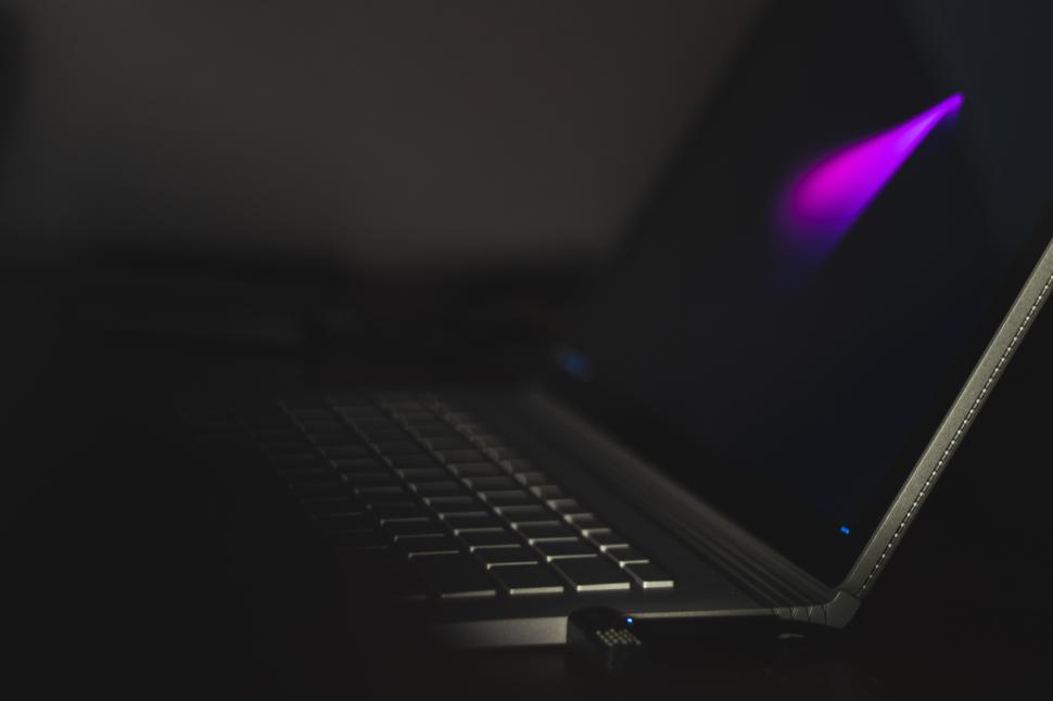 Free Image of Laptop screen glowing with purple light in dark setting 